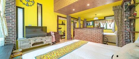 A room with a bed, a television, a brick fireplace, and a yellow wall.
