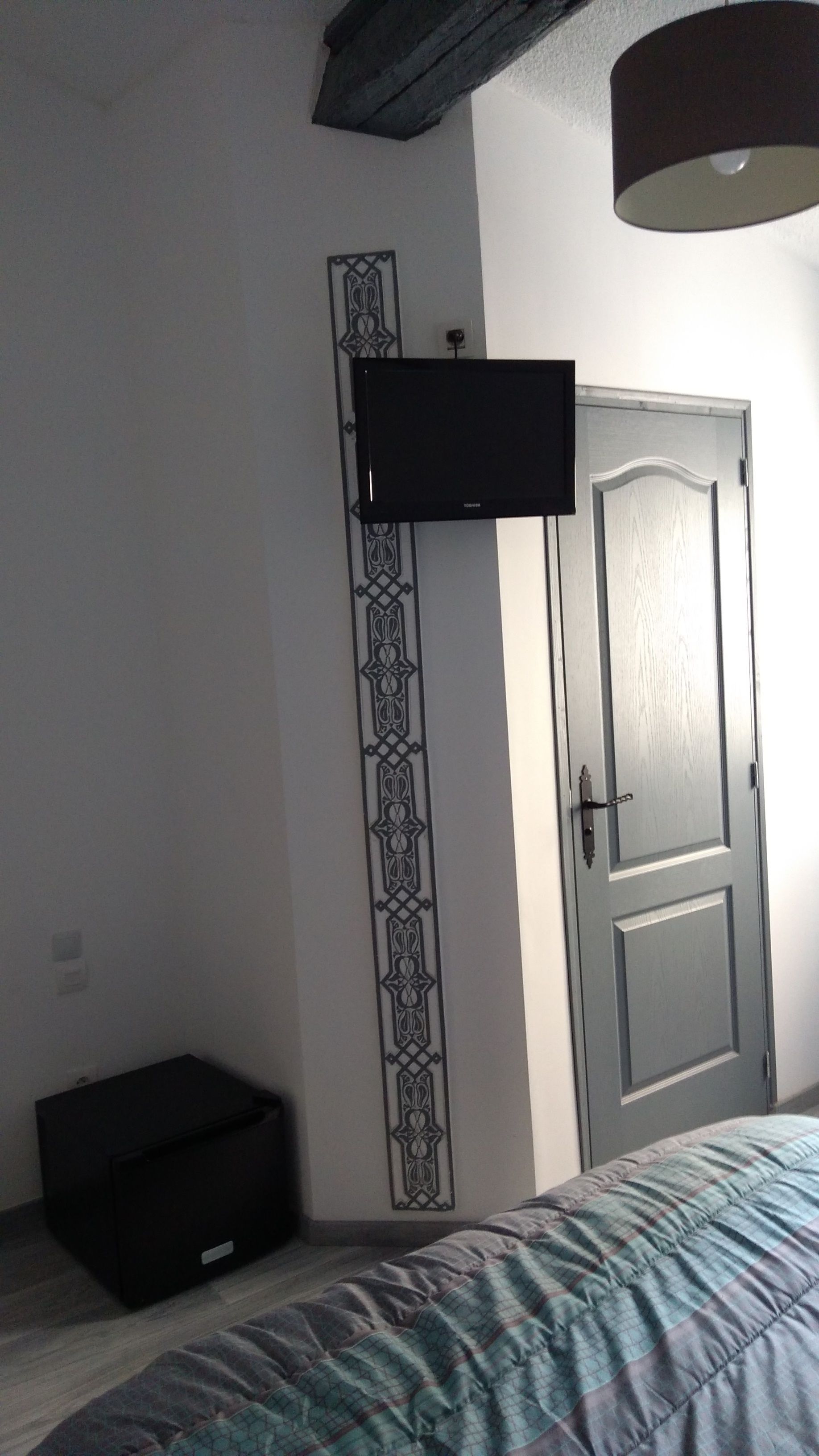 A bedroom with a bed, a television mounted on the wall, a door, and a small black suitcase on the floor.