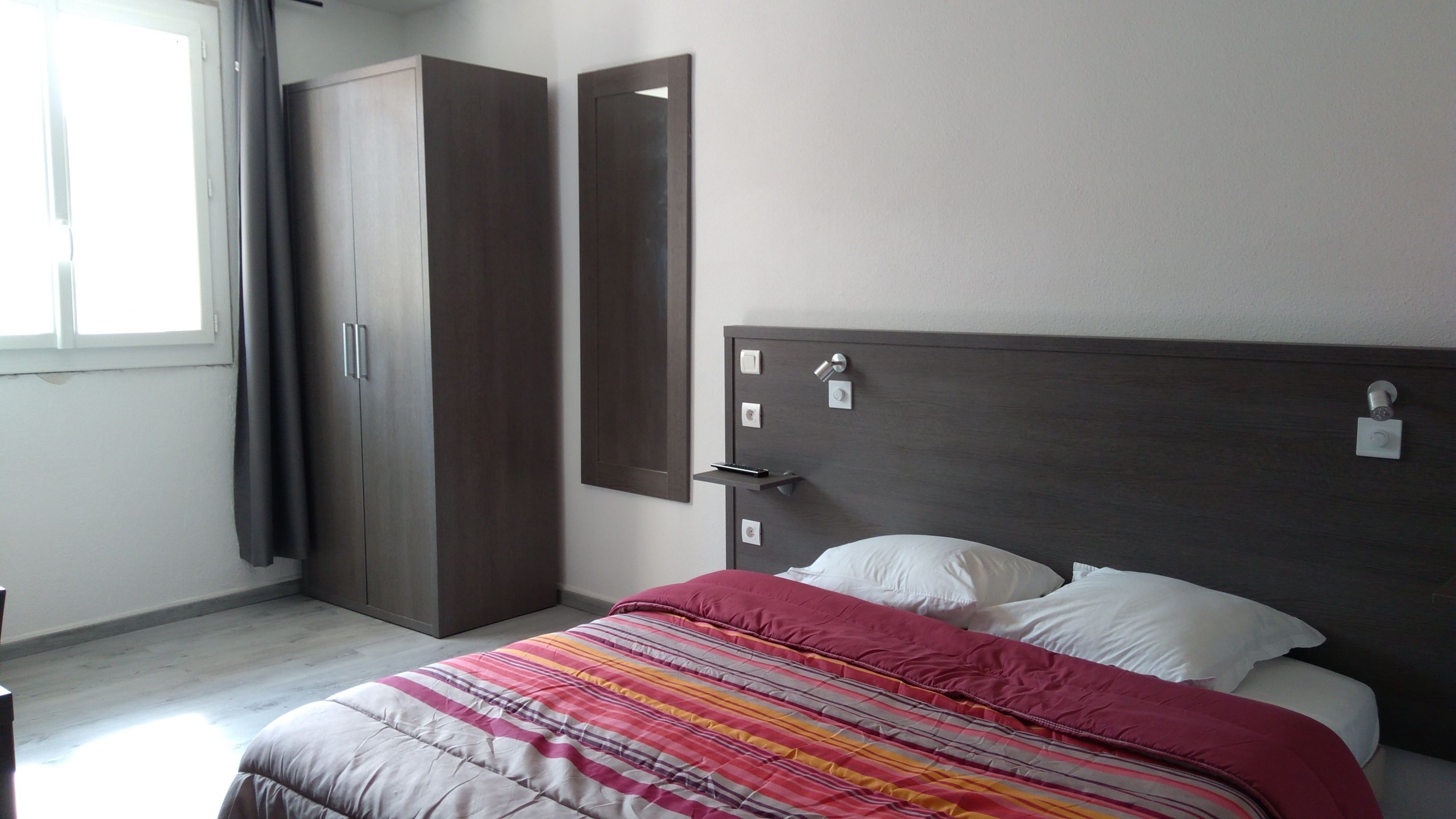A bedroom with a bed, a wardrobe, a mirror, and a window.