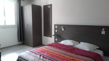 A bedroom with a bed, a wardrobe, a mirror, and a window.
