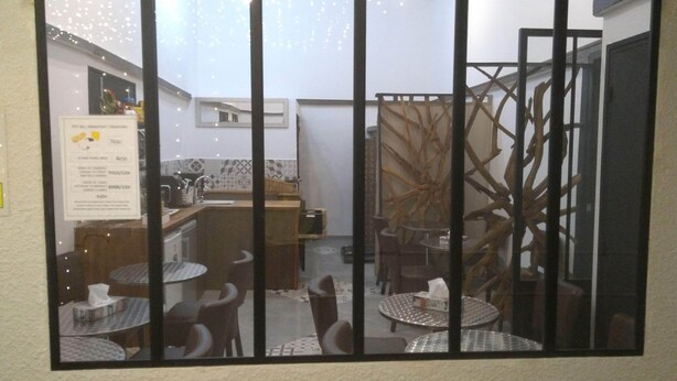 A small, enclosed outdoor dining area with metal tables and chairs, a kitchen area with a tiled backsplash, and a decorative plant. - Mauguio Center Hôtel (Mauguio)