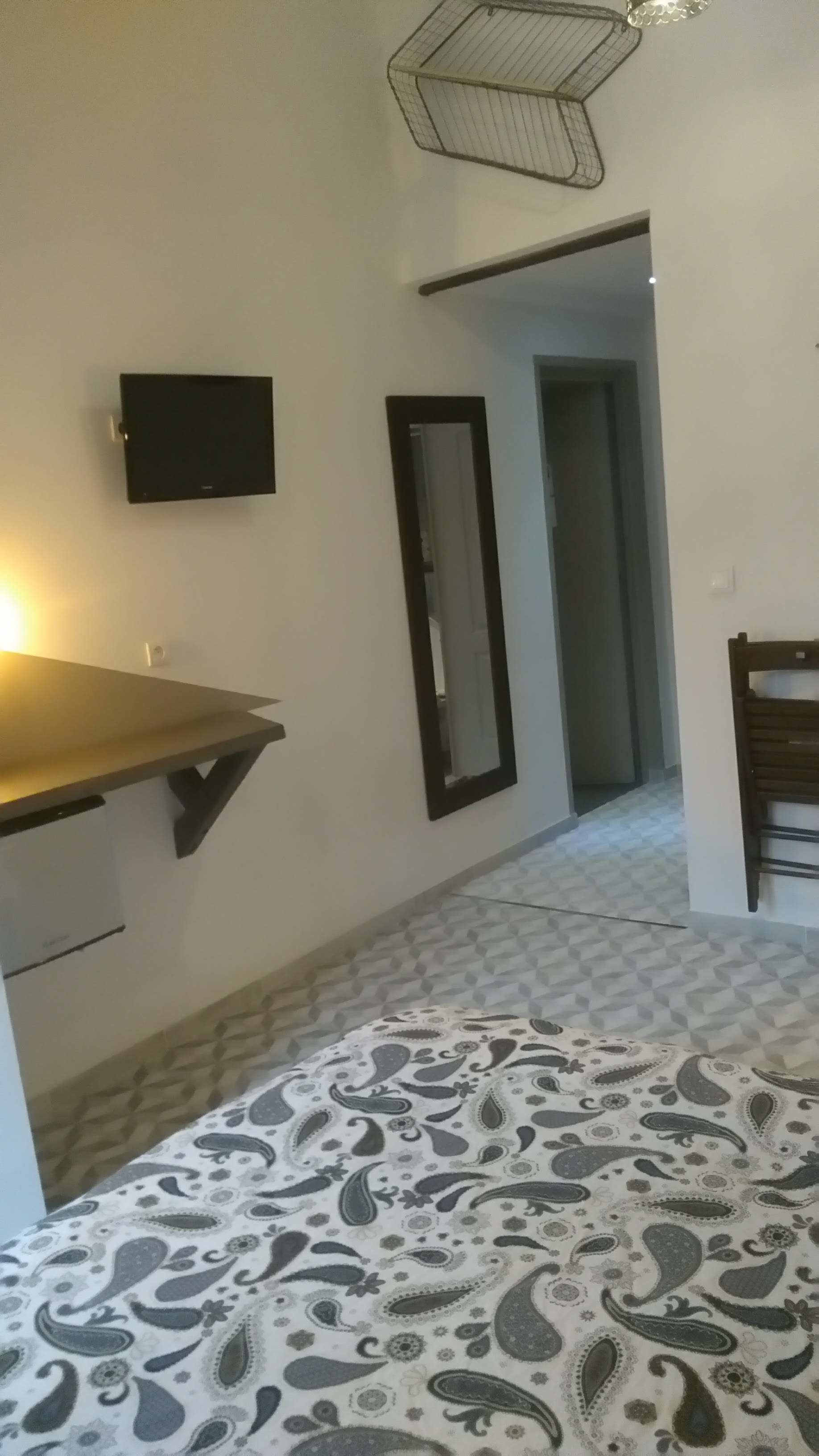 A bedroom with a bed, a desk, a chair, a TV, and a mirror.