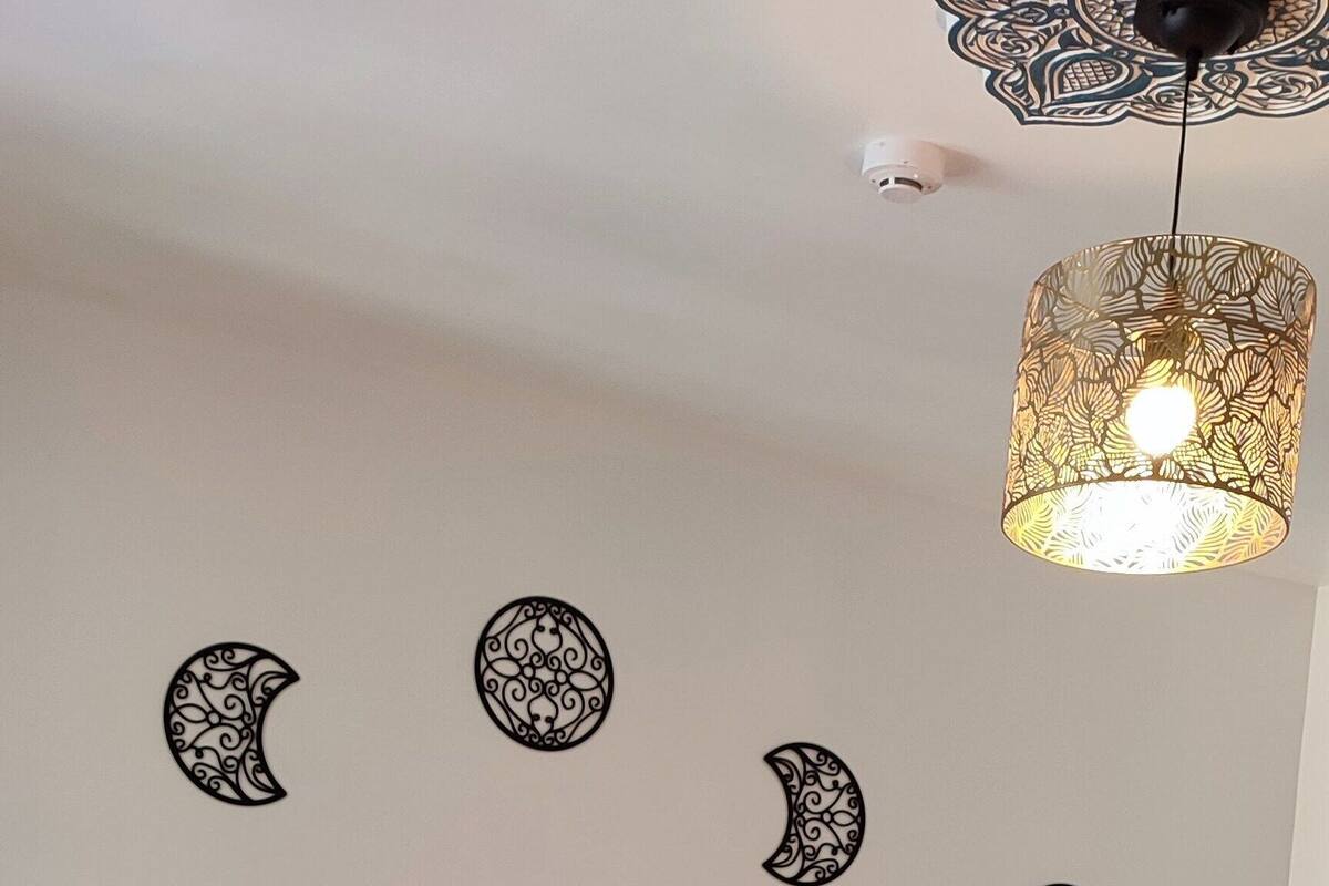 Un dormitorio con cama, ropa de cama estampada, luces fijadas a la pared y una lámpara de techo.