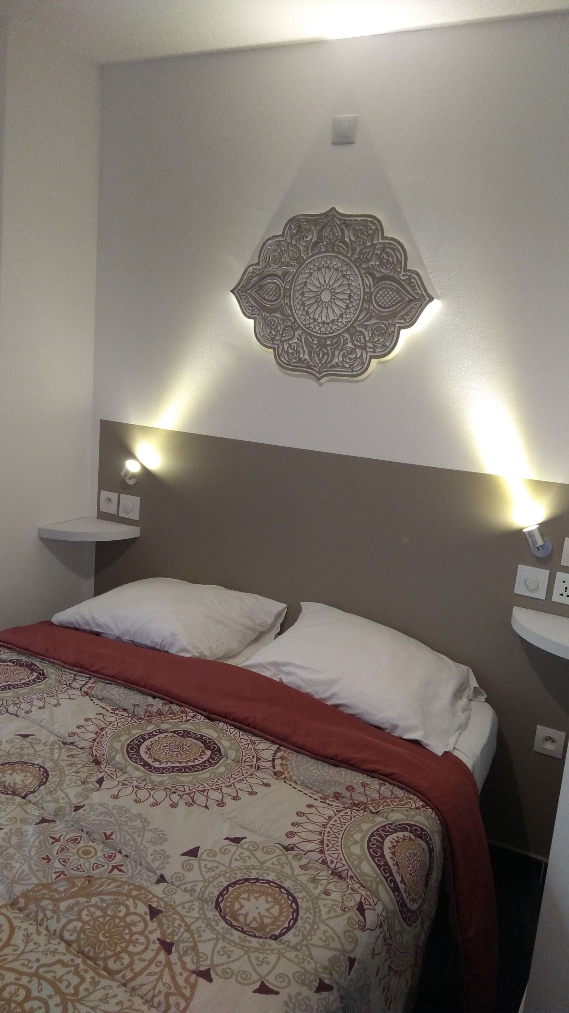 Een hotelkamer met een bed, een decoratief wandobject en bedlampjes.
