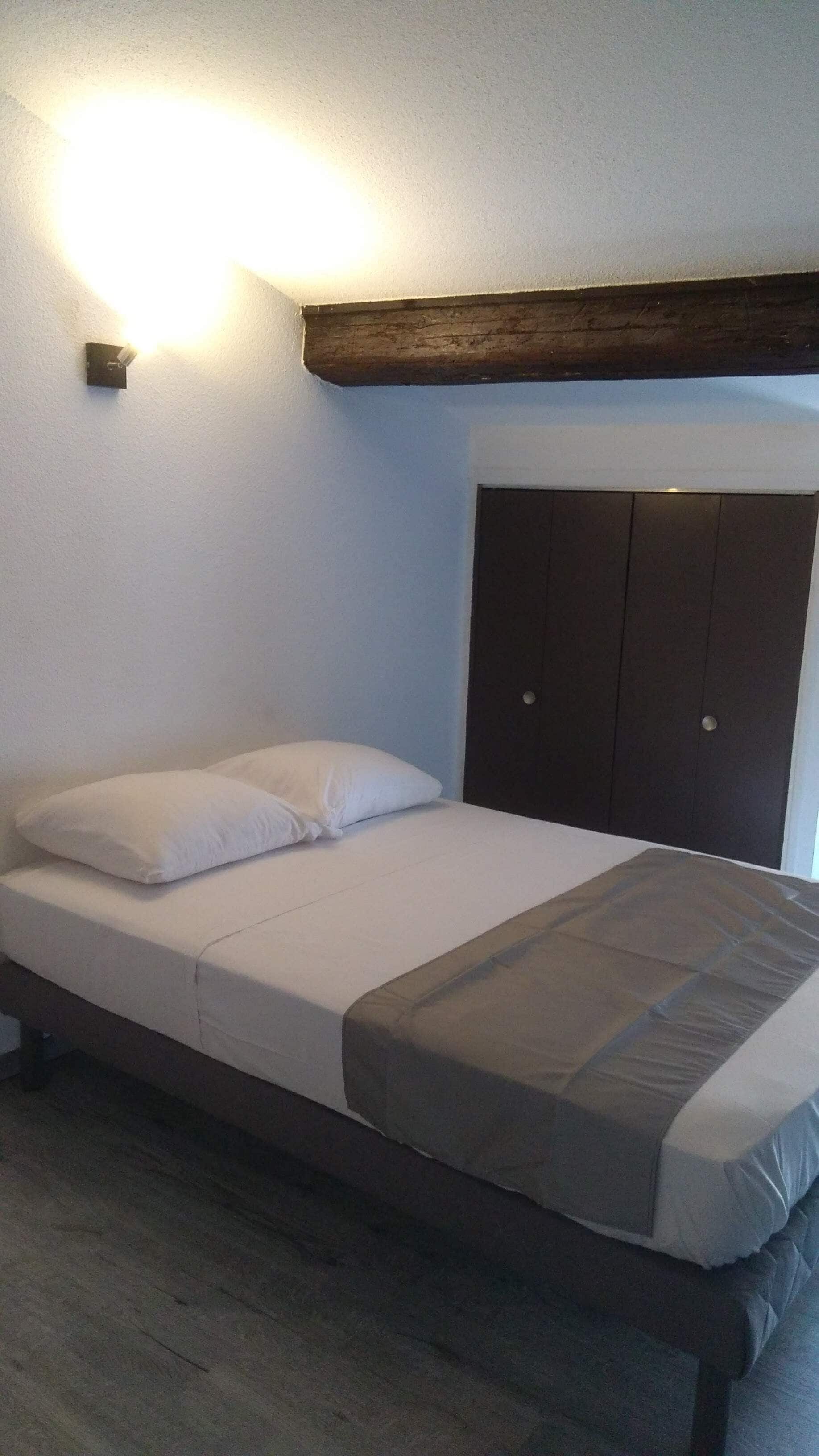 Un dormitorio con cama, almohadas, un armario y una lámpara de pared.