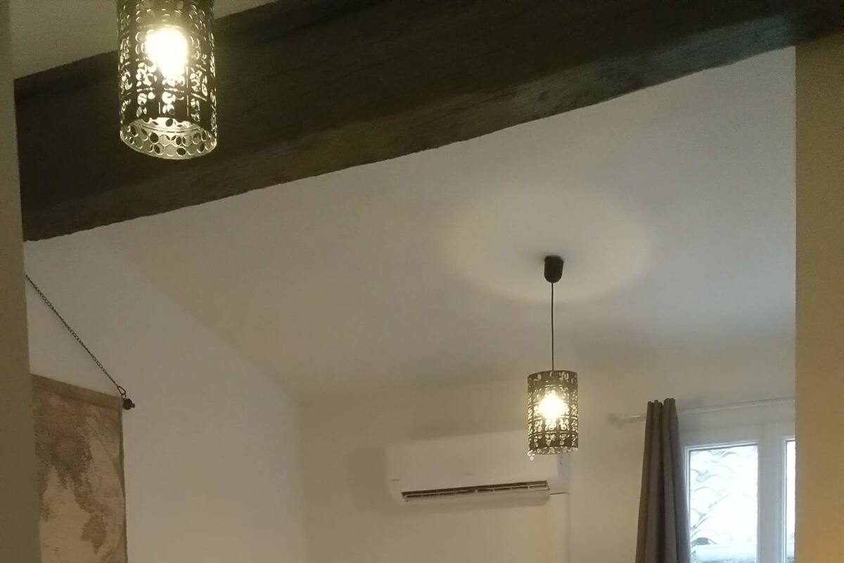 Un dormitorio con colcha estampada, aire acondicionado de pared, lámpara de techo y ventana con cortinas.