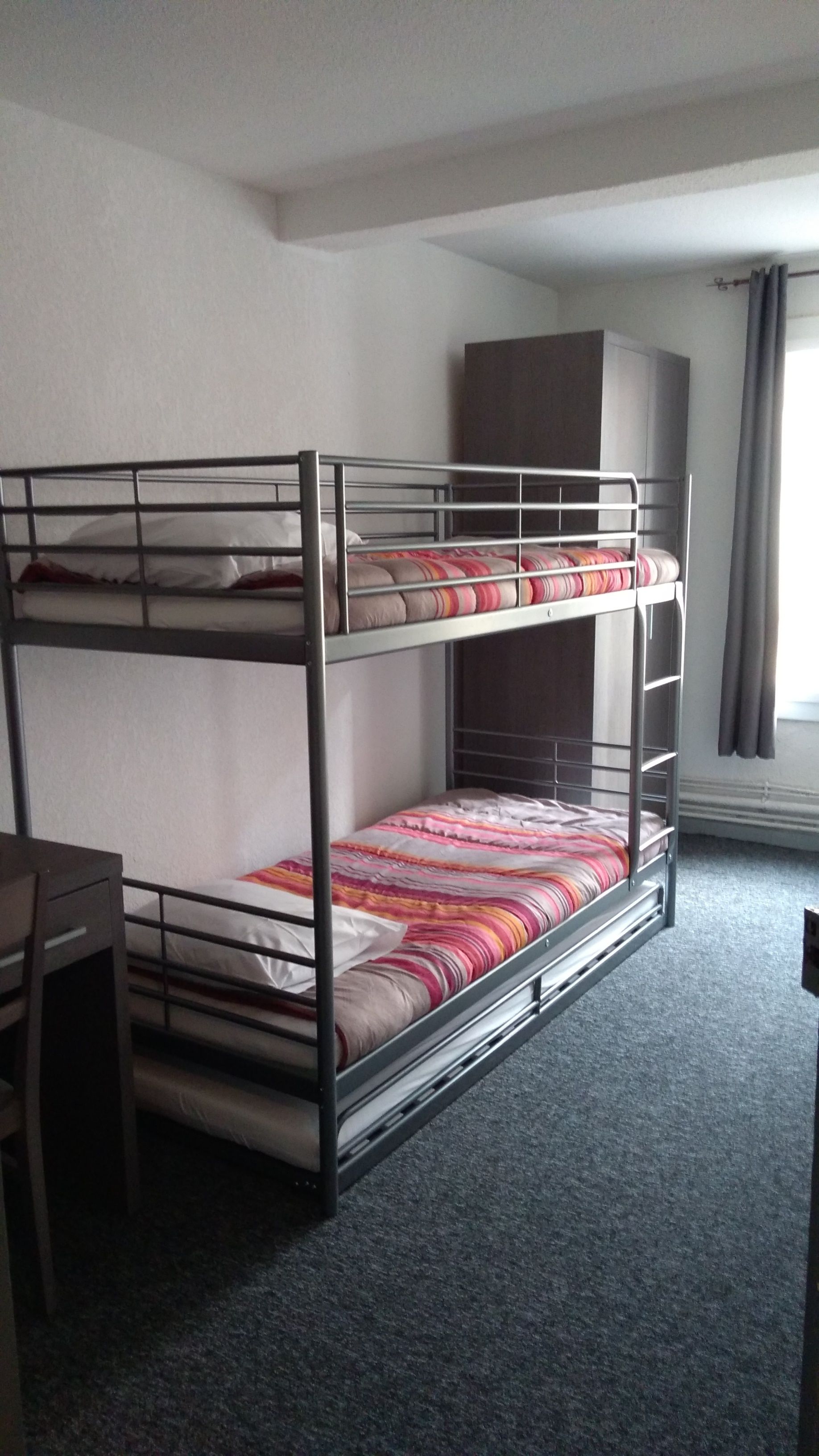Llits superposats amb escriptori i armari en una habitació amb sòl de moqueta.