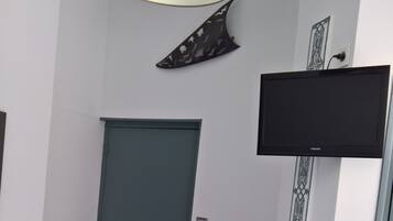 Une pièce avec une porte de couleur turquoise, un meuble noir, un téléviseur fixé au mur et un motif décoratif sur le mur.