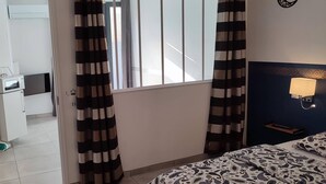 A hotel room with a bed, a bedside lamp, a window with curtains, a small table, and a microwave. - Mauguio Center Hôtel (Mauguio)