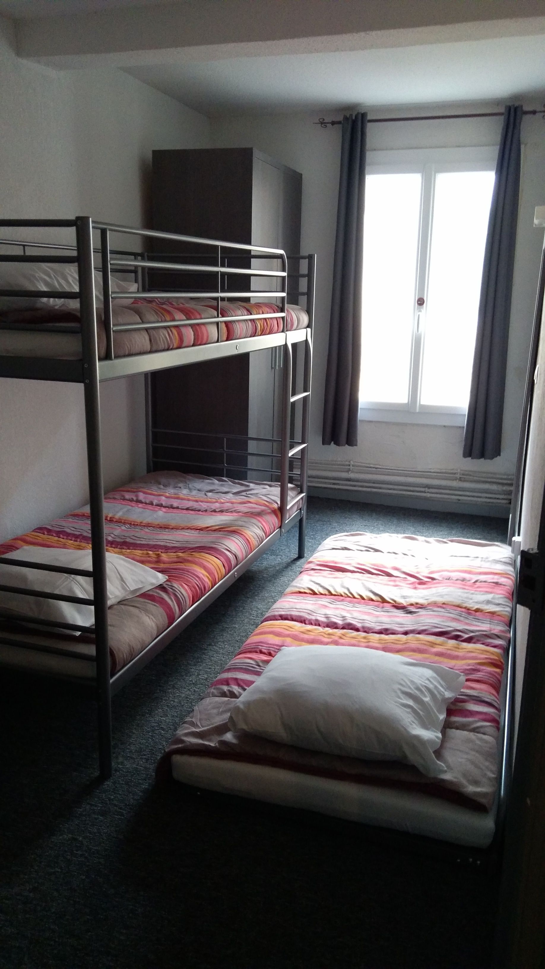 Ein Schlafsaalzimmer mit Etagenbetten, einem Kleiderschrank und einem Fenster mit Vorhängen.