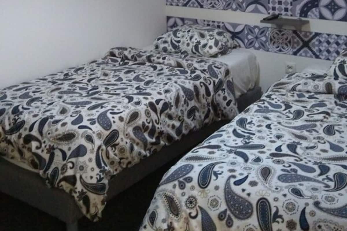 Una habitación con dos camas individuales, un cabecero estampado y una pared lisa.