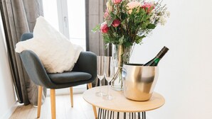 A modern room with a round table, a chair, a fluffy rug, a vase with flowers, and a champagne bottle.