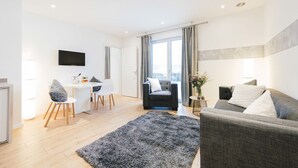 A modern living room with a grey sofa, a black rug, and a dining area with a white table and chairs.