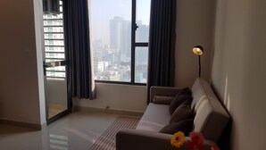 A modern living room with a sofa, a lamp, and a view of a cityscape through large windows. - Herla Central Saigon (Ho Chi Minh City)