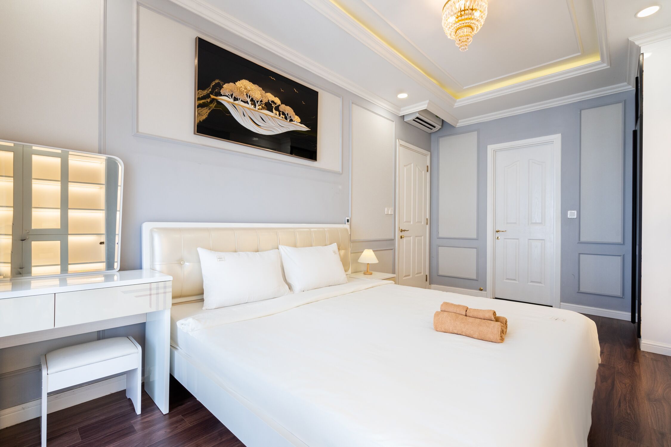 A hotel room with a large bed, a bedside table with a lamp, a desk with a mirror, and a painting on the wall.