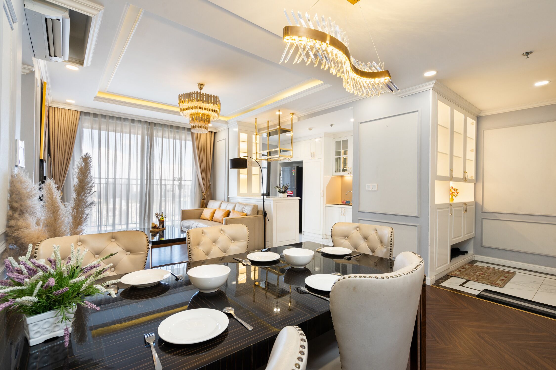 A modern dining area with a glass table, white chairs, and a chandelier.