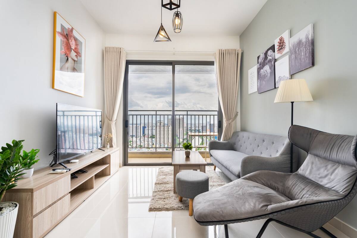 A modern living room with a grey sofa, a TV, and a balcony with a city view.