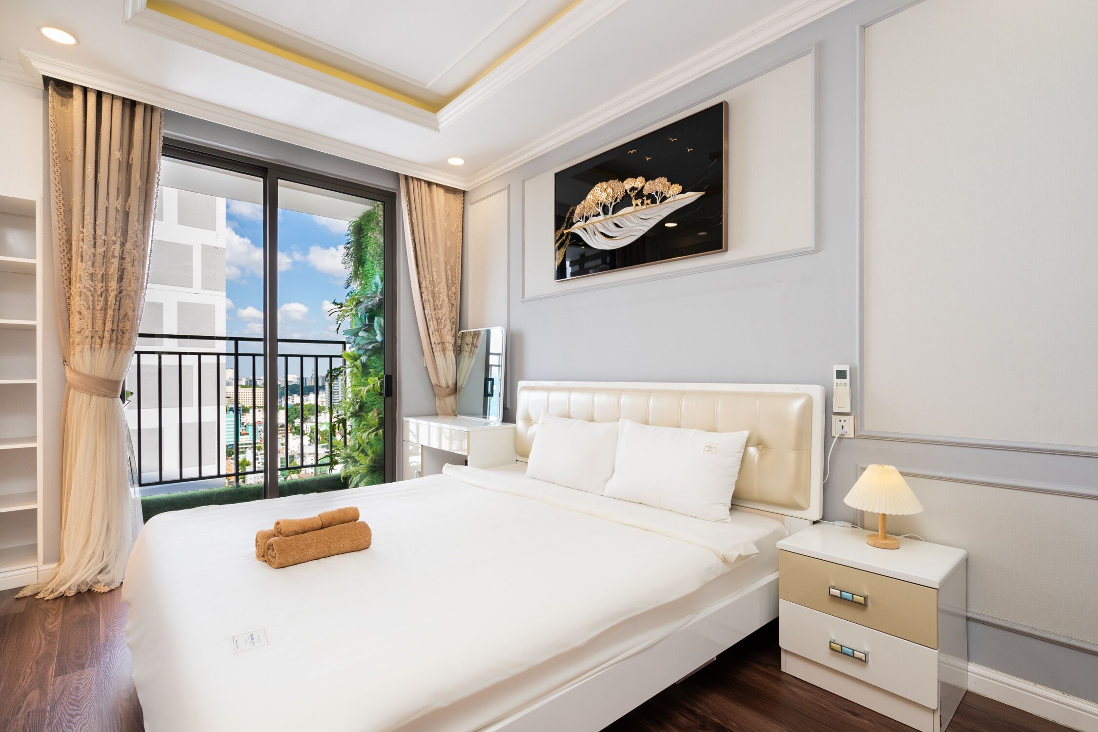 Une chambre d’hôtel avec un grand lit, une table de chevet avec une lampe, une fenêtre avec des rideaux et un tableau au mur.
