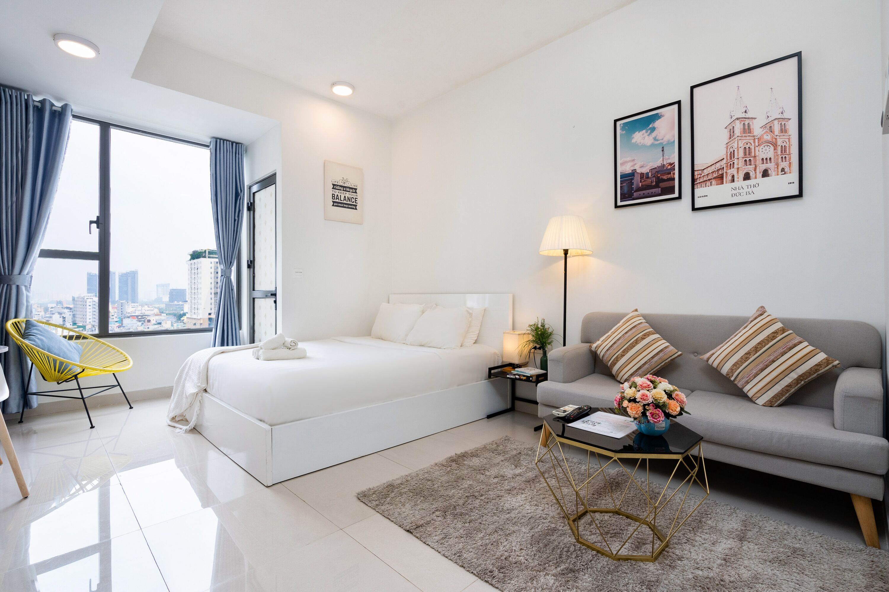A modern hotel room with a large bed, a sofa, a coffee table, and a view of the city.