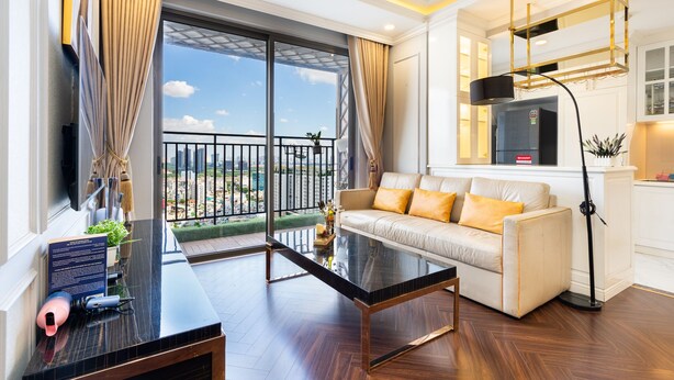 A modern living room with a glass coffee table, a sofa with yellow cushions, a flat-screen TV, and a balcony with a view of the city. - TeeUP Home (Ho Chi Minh City)