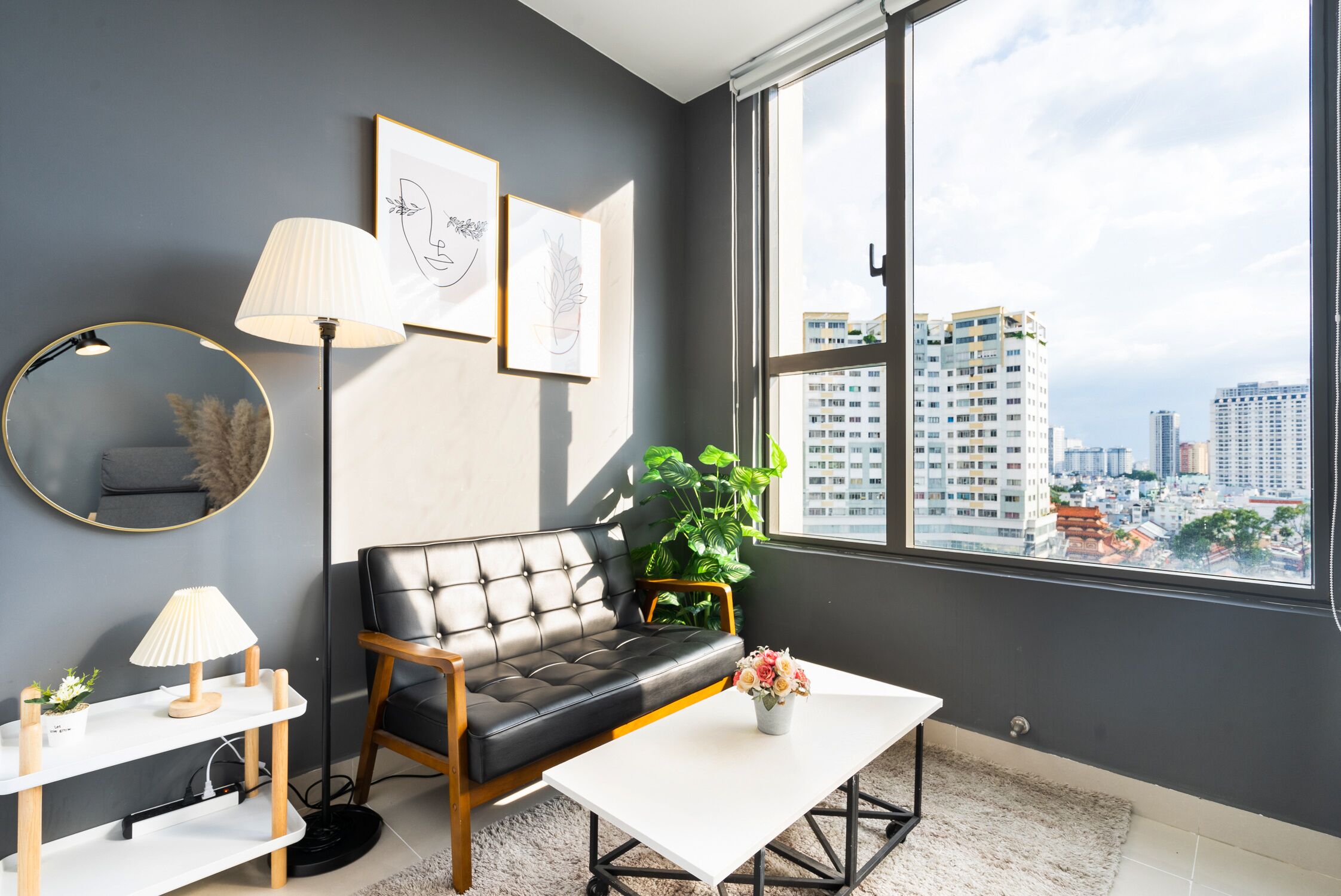 A modern living room with a sofa, a coffee table, a lamp, and a large window with a city view.