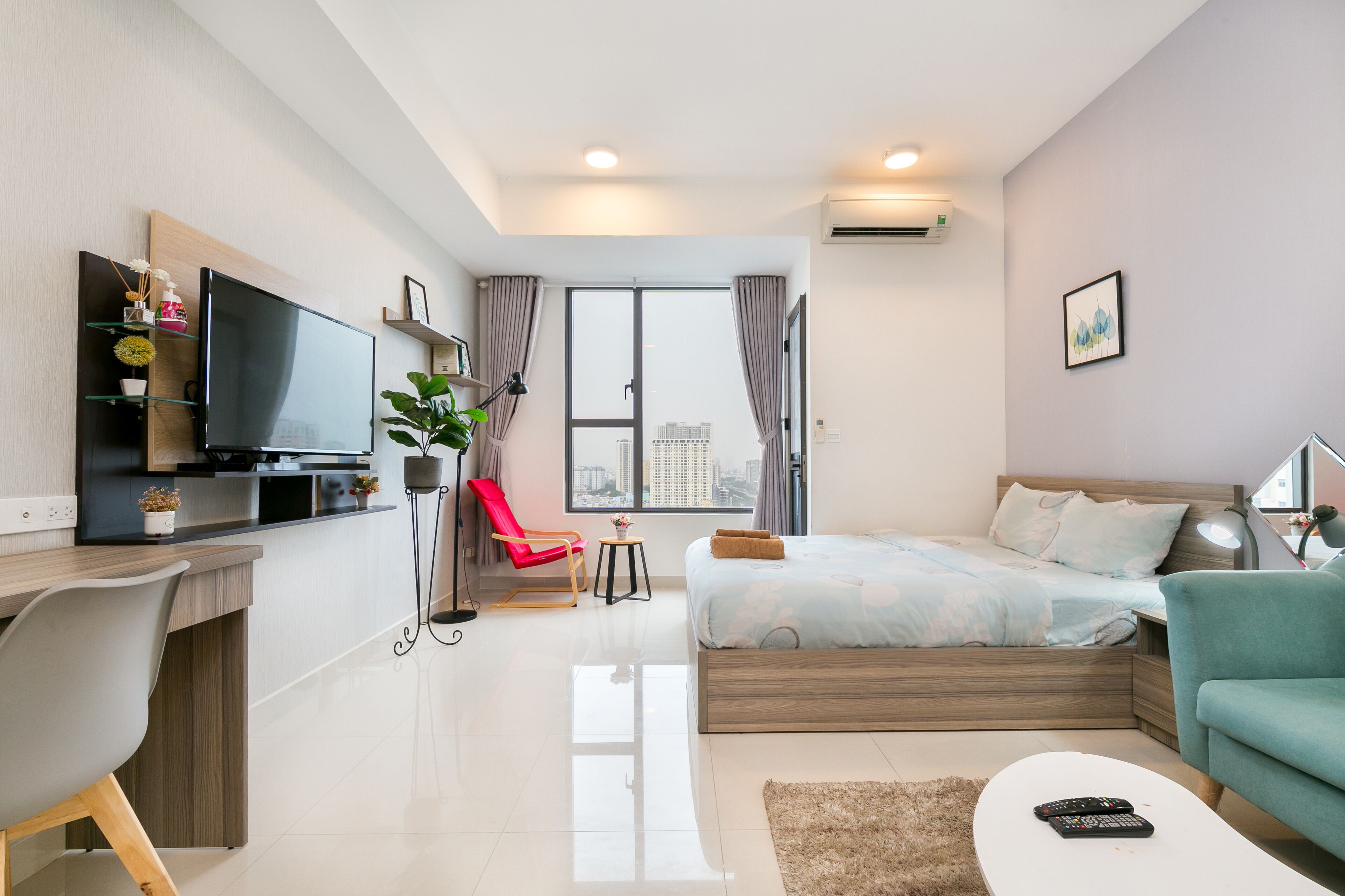 A modern hotel room with a bed, a desk, a TV, and a view of the city.