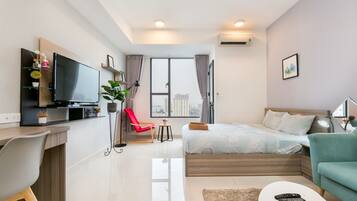A modern hotel room with a bed, a desk, a TV, and a view of the city.