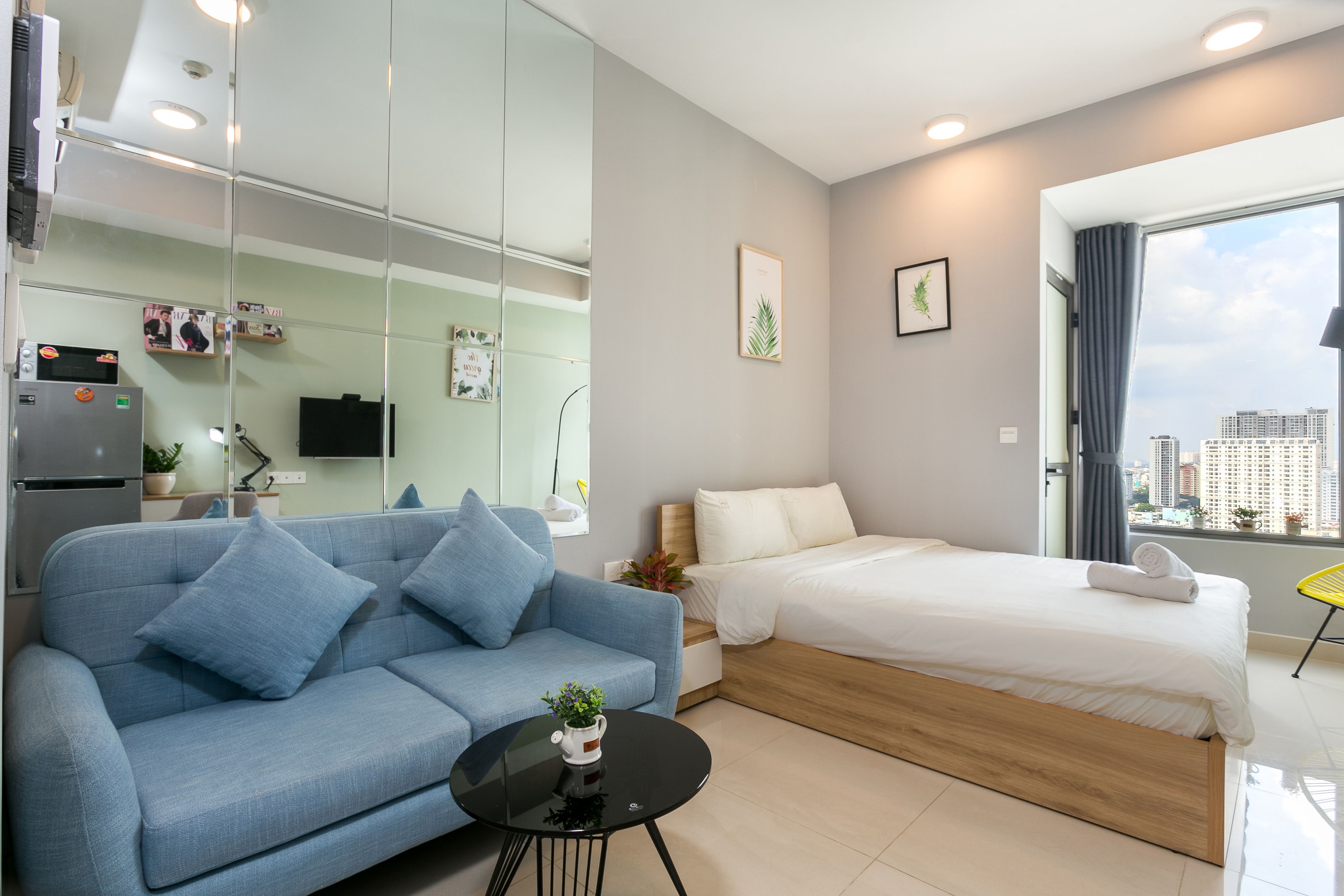 Una habitación de hotel moderna con sofá, cama, una mesita con planta y vistas a la ciudad desde la ventana.