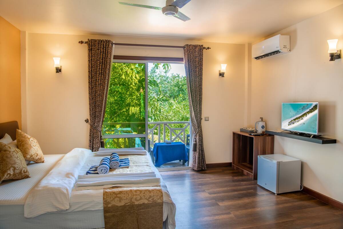Une chambre d’hôtel avec un lit, une télévision, un bureau et une vue sur la verdure environnante.