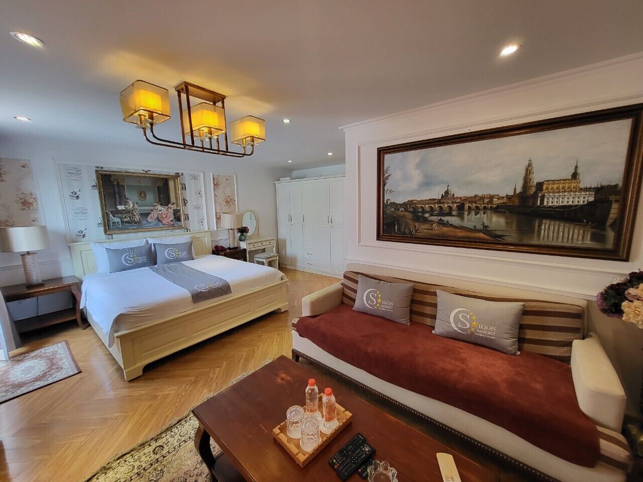 Een hotelkamer met een bed, een bank, een bijzettafeltje en een schilderij van een stadsgezicht.