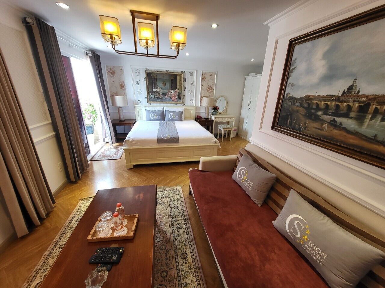 A hotel room with a bed, a sofa, a coffee table, and a painting on the wall.