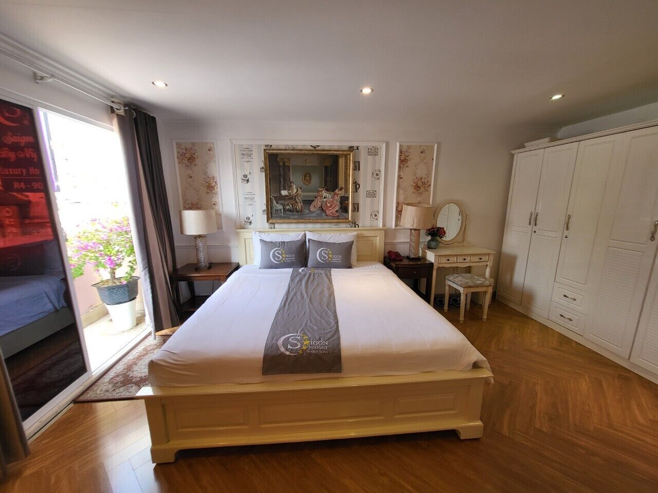 A spacious bedroom with a large bed, a desk, a chair, a wardrobe, and a mirror.