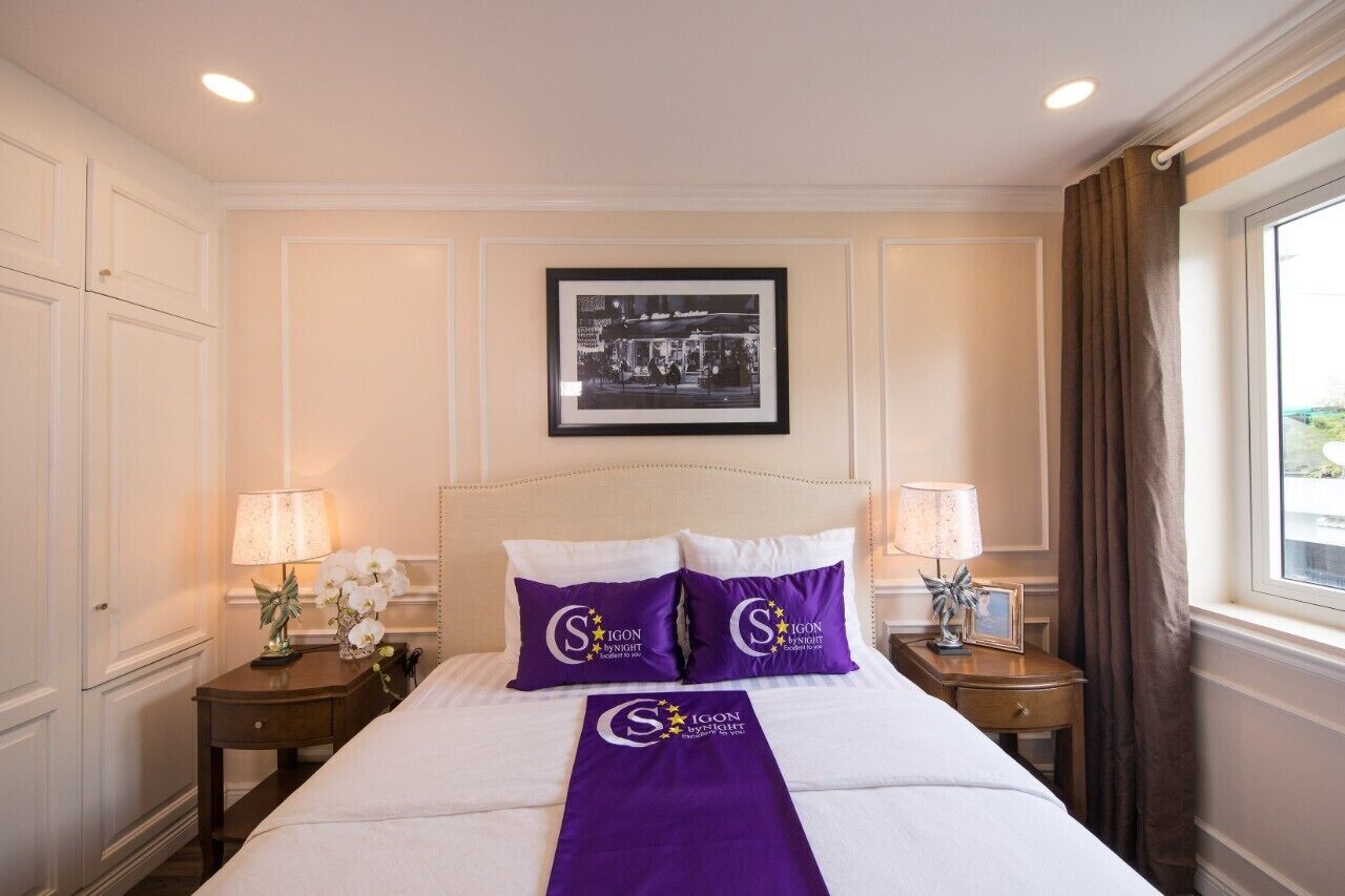 A hotel room with a large bed, two nightstands, a framed picture on the wall, and a window with curtains.