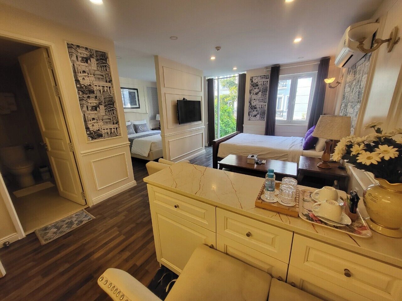 A hotel room with a bed, bedside table, dresser, and a large window.