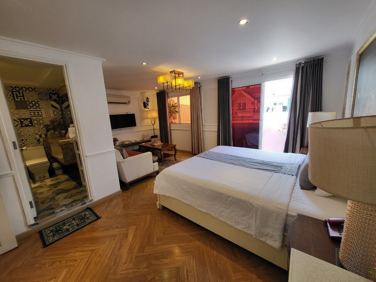 A hotel room with a large bed, a desk, a chair, a TV, and a view of the outside.