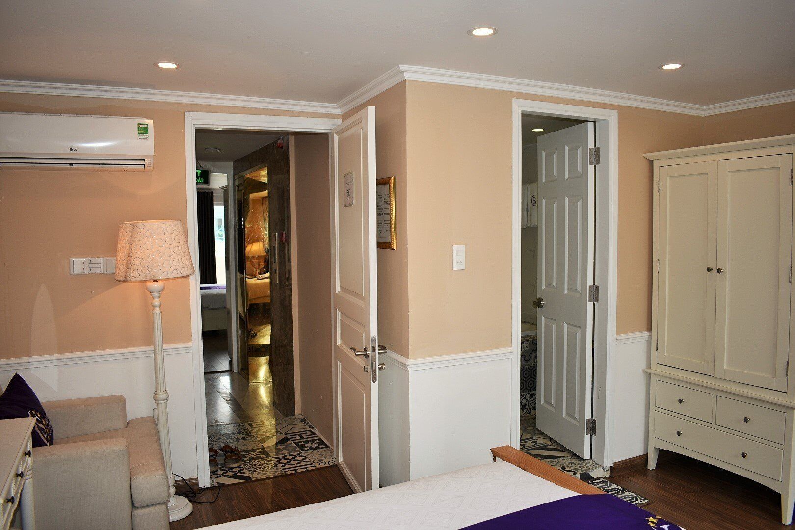 A hotel room with a bed, a wardrobe, a lamp, and a door leading to a hallway.