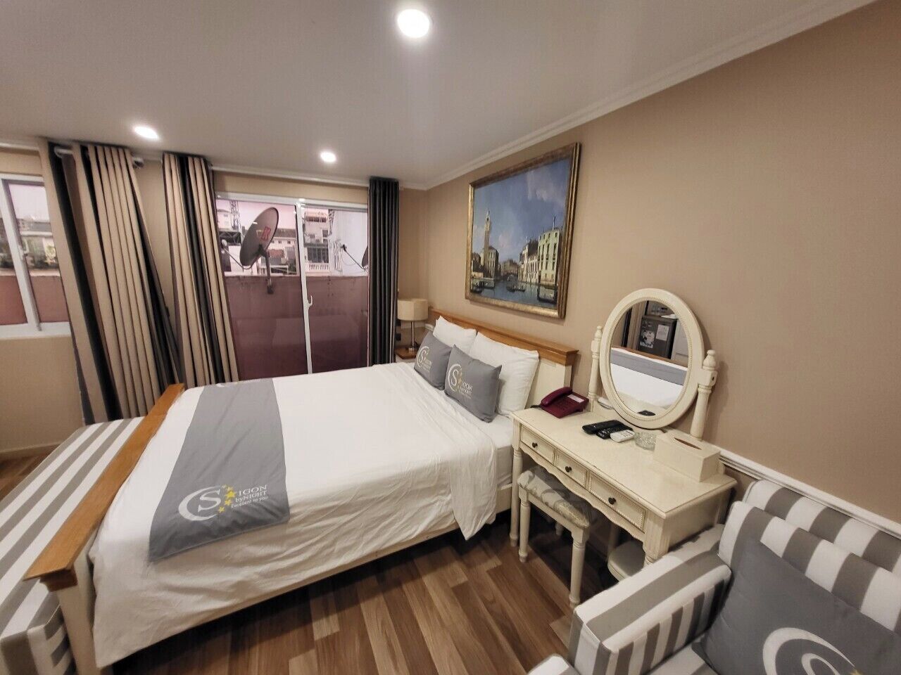 A hotel room with a bed, a desk, a chair, a mirror, and a painting on the wall.