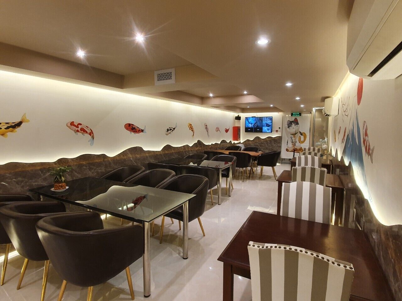 A restaurant with a modern interior, featuring black and white striped chairs, a glass table, and a wall decorated with fish illustrations.