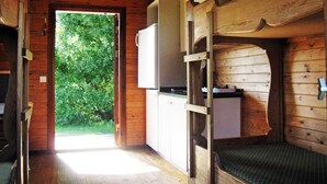 Une cabane en bois avec des lits superposés, un coin cuisine et une porte donnant sur un jardin.