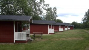 A row of red cabins with white railings and a picnic table in front. - Falkudden Camping (By Kyrkby)