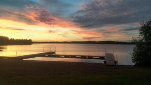 A lakeside view with a wooden dock extending into the water, surrounded by grassy areas and trees. - Falkudden Camping (By Kyrkby)