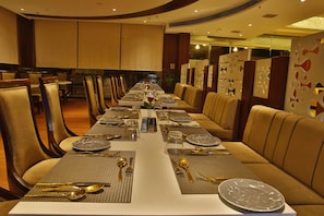 Een lange eettafel gedekt met gouden bestek en borden, omringd door lederen stoelen in een goed verlichte kamer met een modern design.