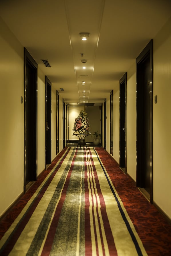 Een hotelgang met een rood tapijt, deuren aan beide kanten en een kerstboom in het midden.