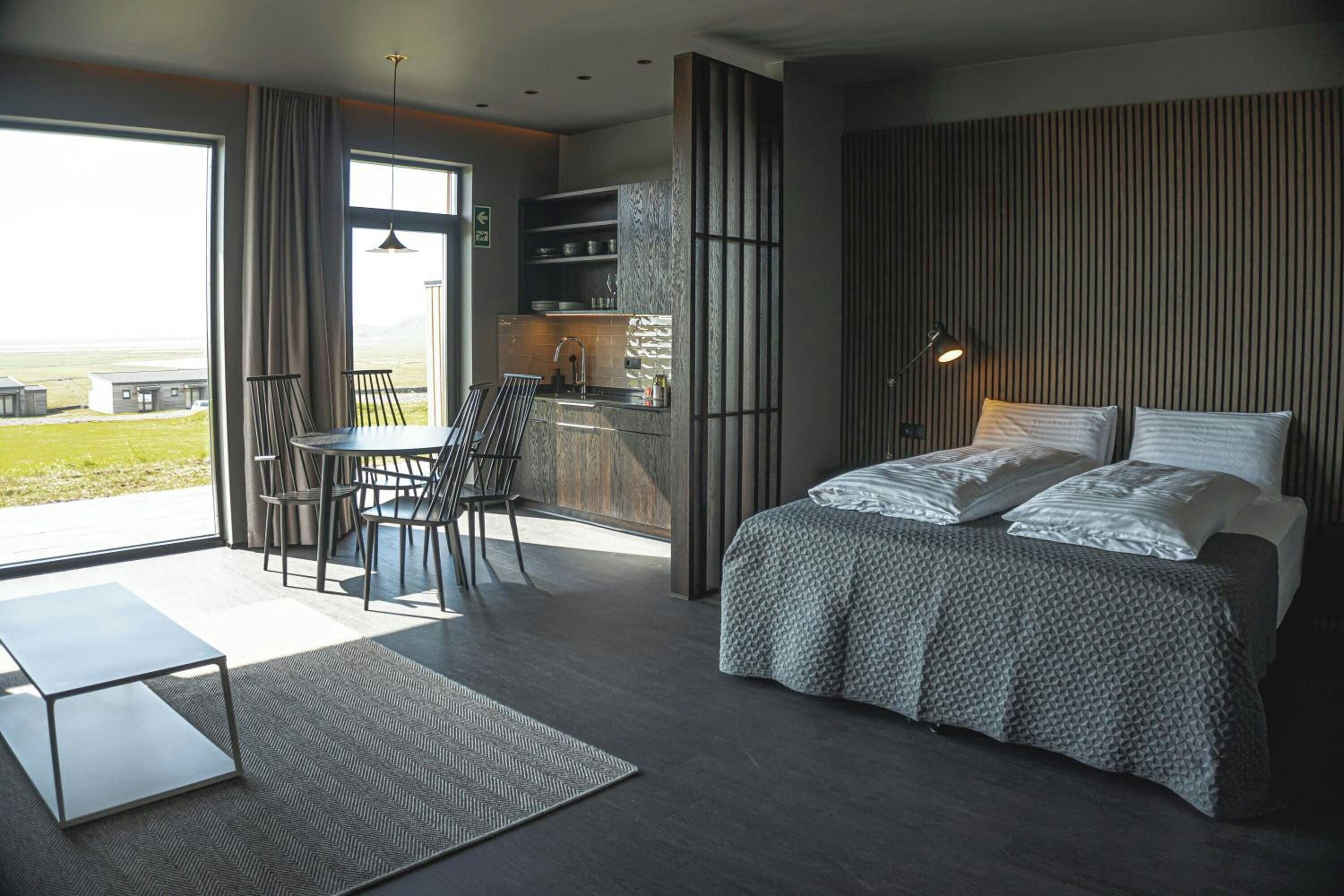 A modern bedroom with a large bed, a desk, and a view of the outdoors.