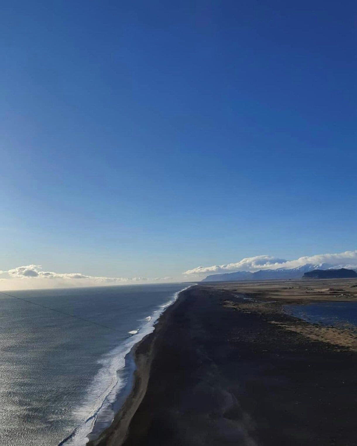 A coastal landscape with a beach and distant mountains.