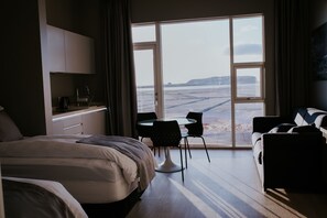 A hotel room with a bed, a desk, a chair, and a view of the beach. - Black Beach Suites (Vik I Myrdal)