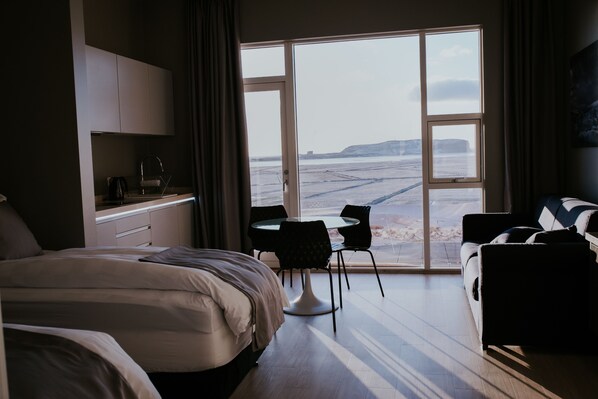 A hotel room with a bed, a desk, a chair, and a view of the beach.