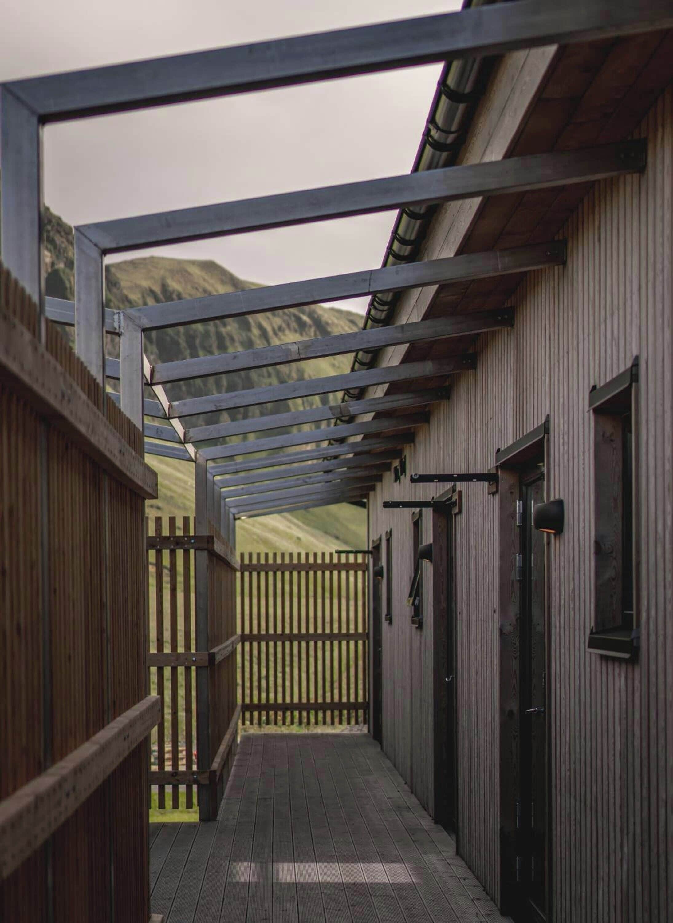 A corridor with wooden railings, a metal roof structure, and a view of a mountainous landscape.