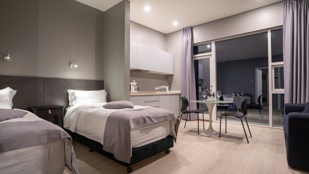 A modern hotel room with a large bed, a desk, and a dining area. - Black Beach Suites (Vik I Myrdal)
