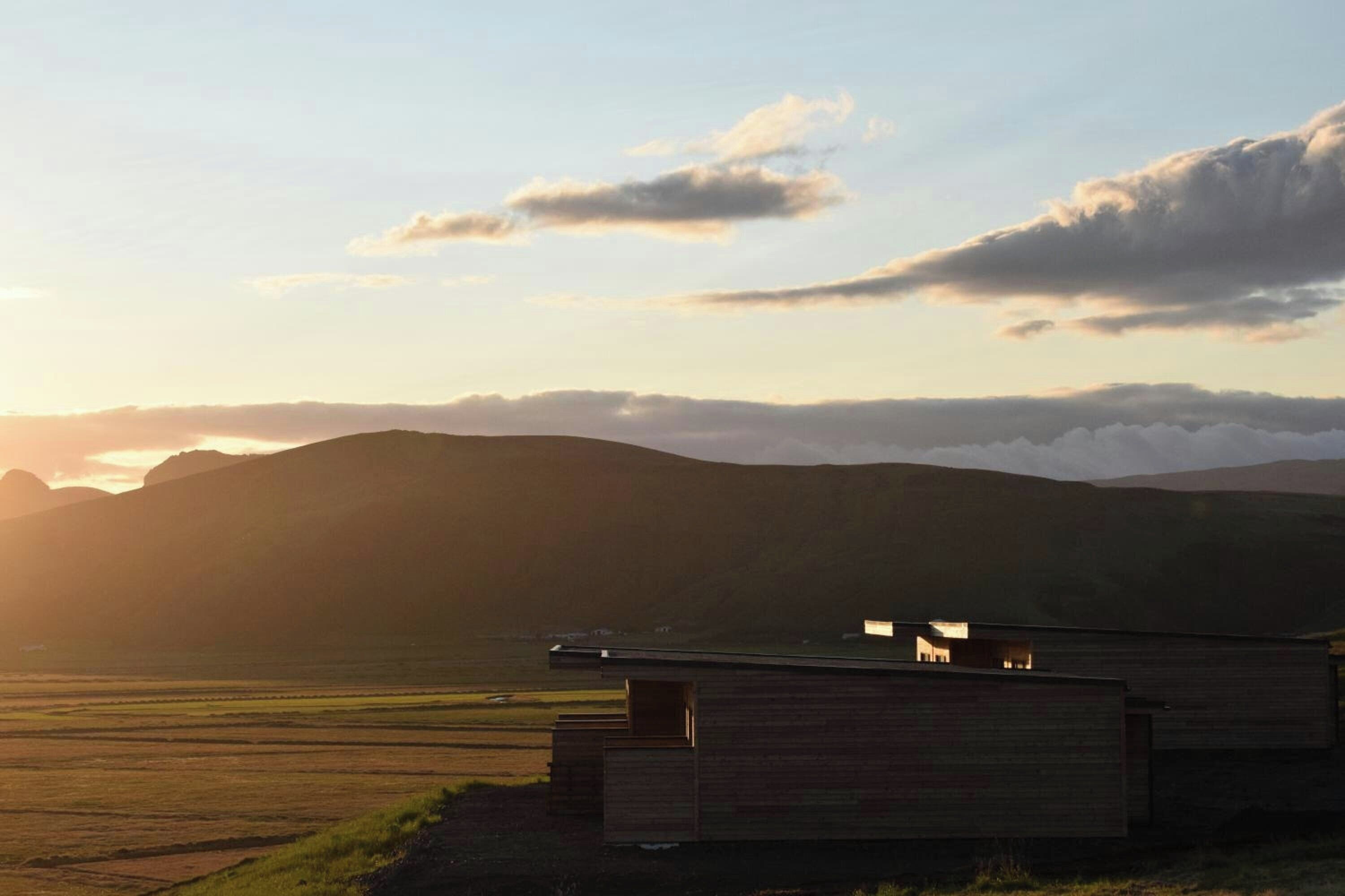 A building with a flat roof and a small porch area, situated in a rural landscape with open fields and distant hills.